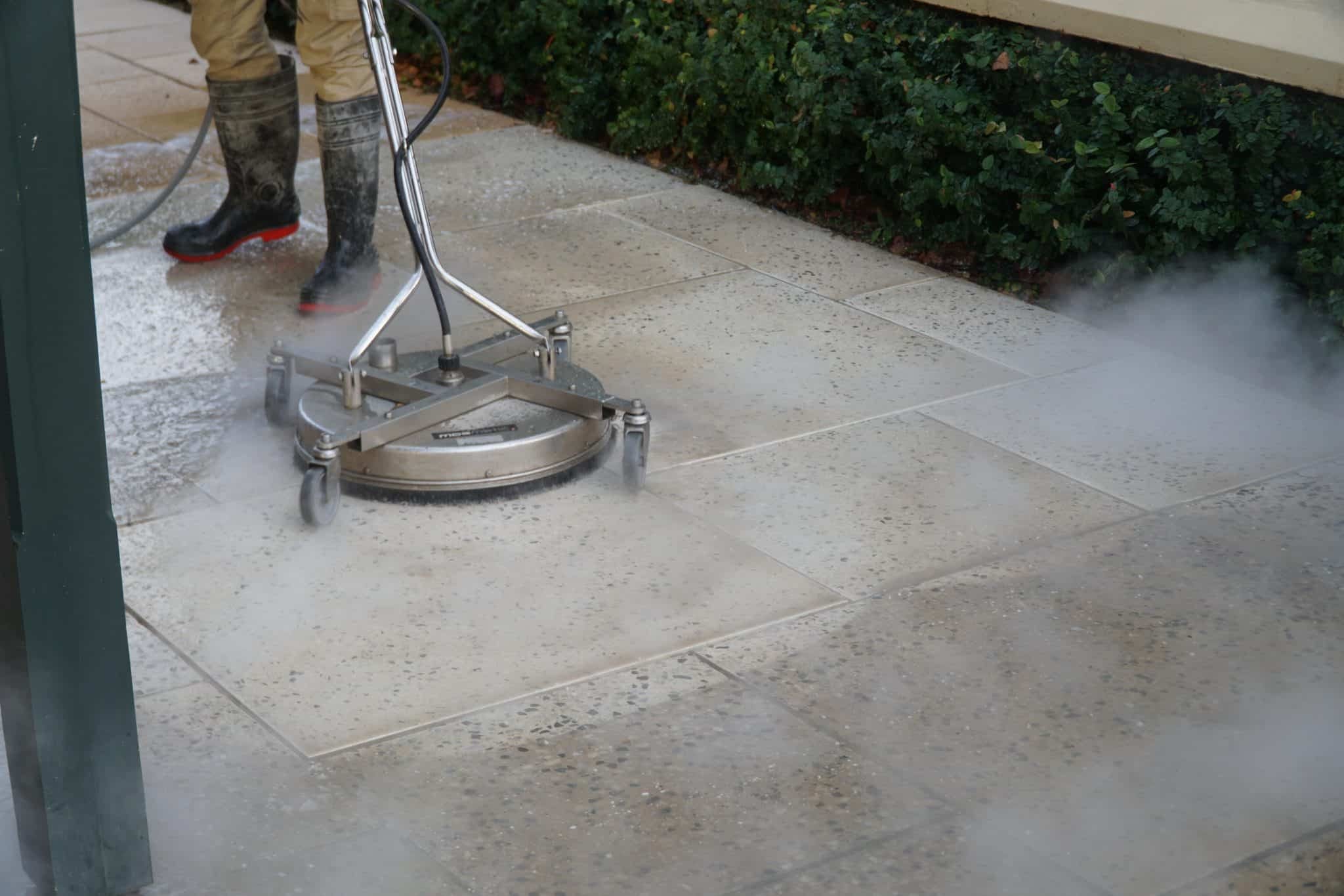 Worker using a steam pressure cleaner on paving stones