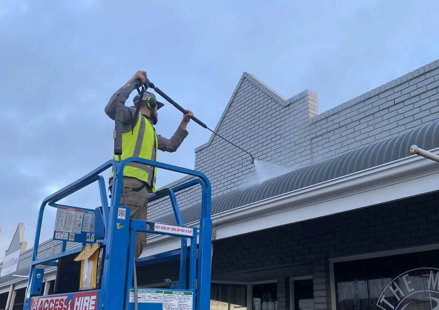 Worker performing pre-paint cleaning on a building exterior using a pressure washer in Adelaide.